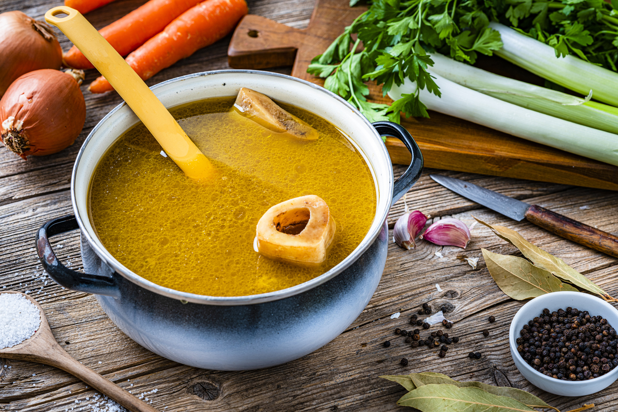 High angle view of a cooking pan filled with homemade bone broth shot on rustic wooden table. Ingredients for cooking bone broth are all around the pan. High resolution 42Mp studio digital capture taken with Sony A7rII and Sony FE 90mm f2.8 macro G OSS lens