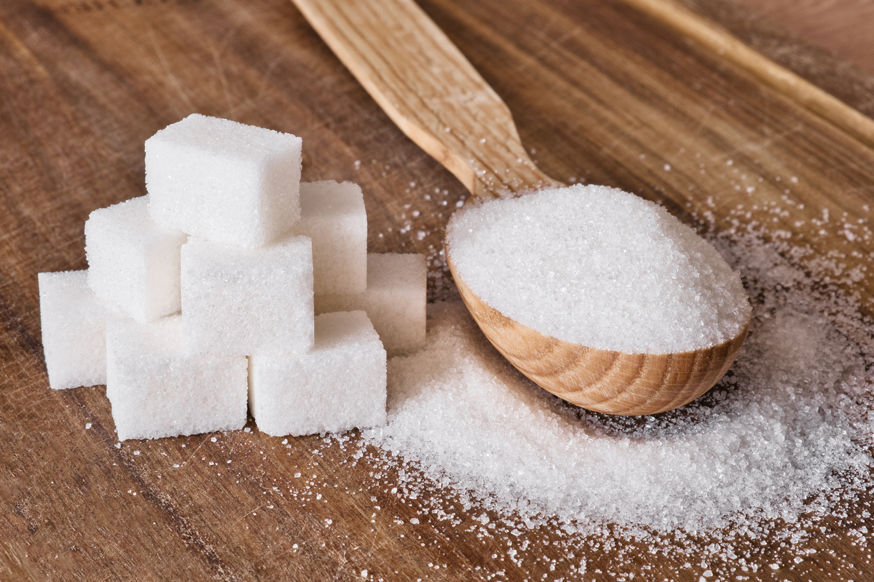 Granulated sugar in wooden spoon and sugar cubes stacked in pyramid on wooden background. Selective focus.